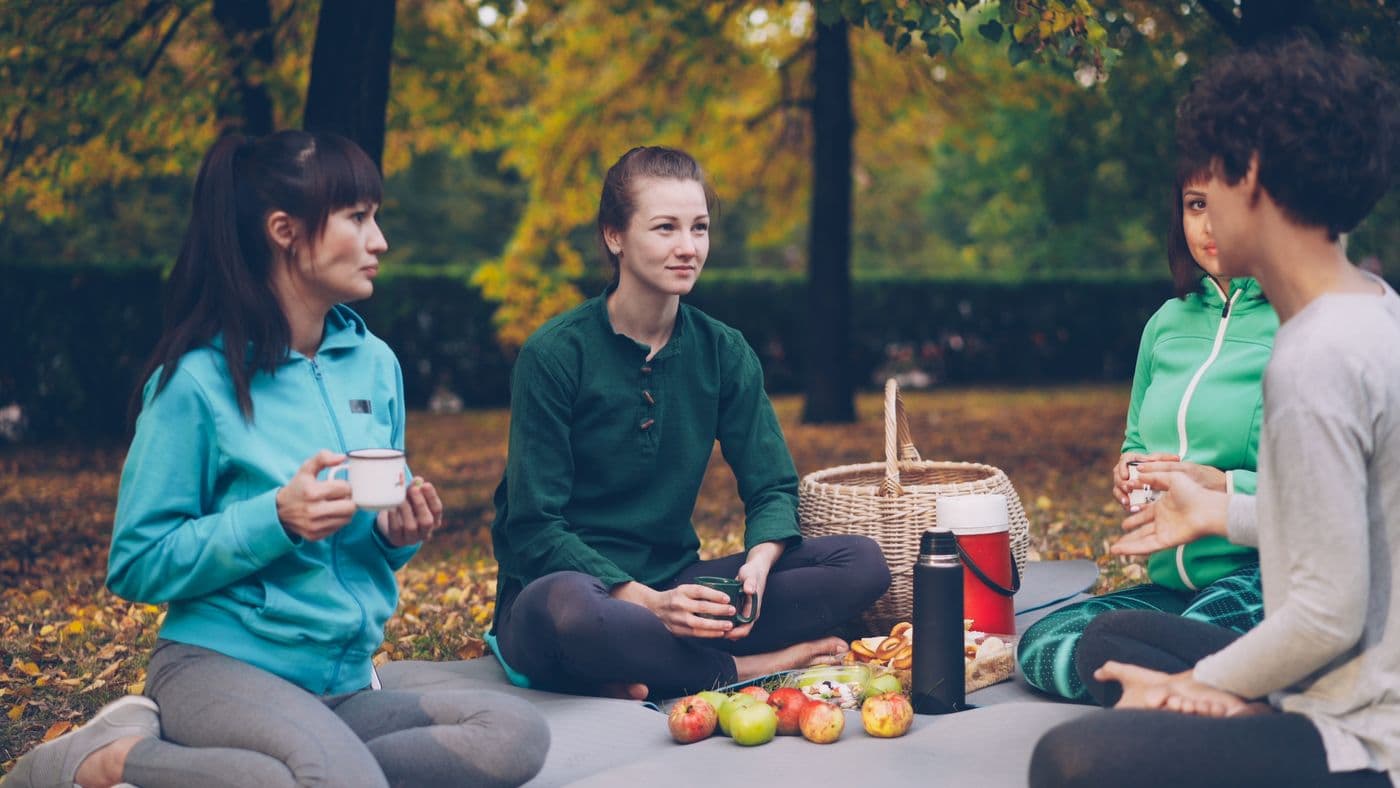 Parkta piknik örtüsü üzerinde sohbet eden bir grup kadın